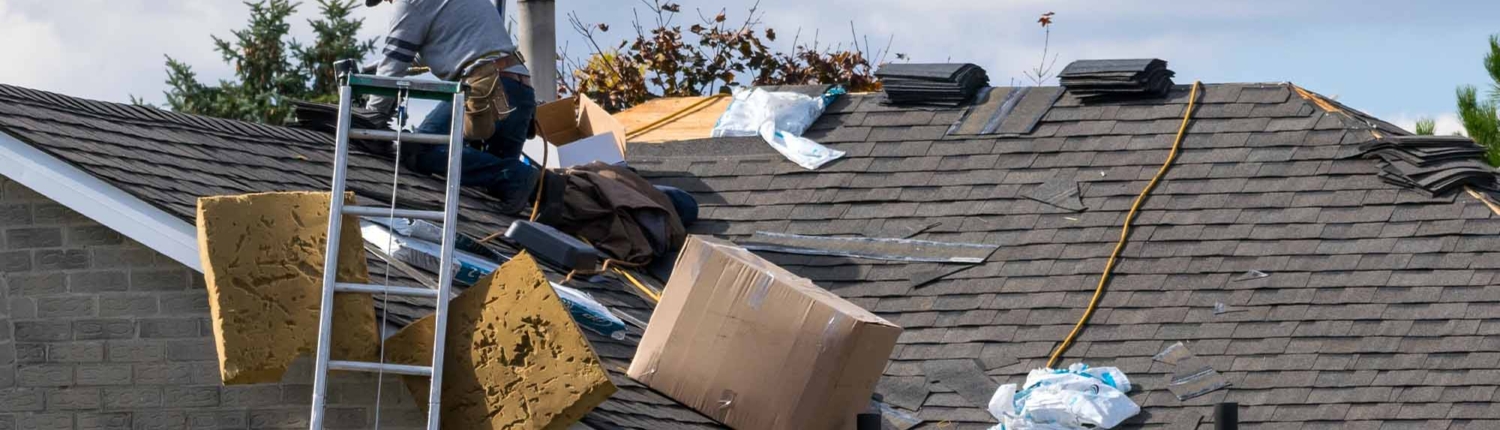 Worker on the roof of a 2-storey family house installing new asphalt shingles