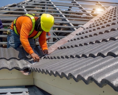 Image of a worker replacing tiles on a residential roof.