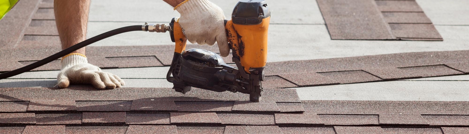 Image of a worker nailing shingles onto a commercial roof.